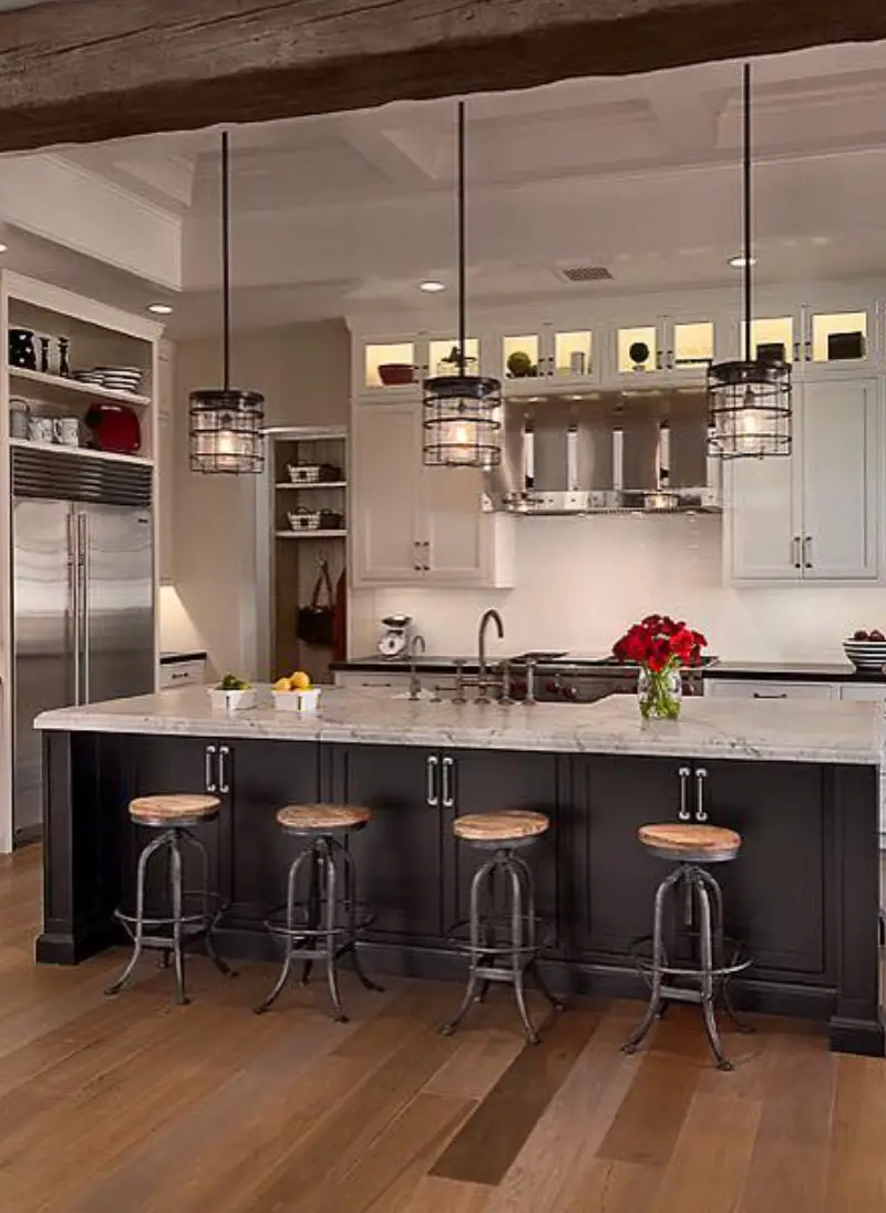 Modern kitchen featuring white cabinetry, a marble island with four stools, pendant lights, and stainless steel appliances in warm tones.